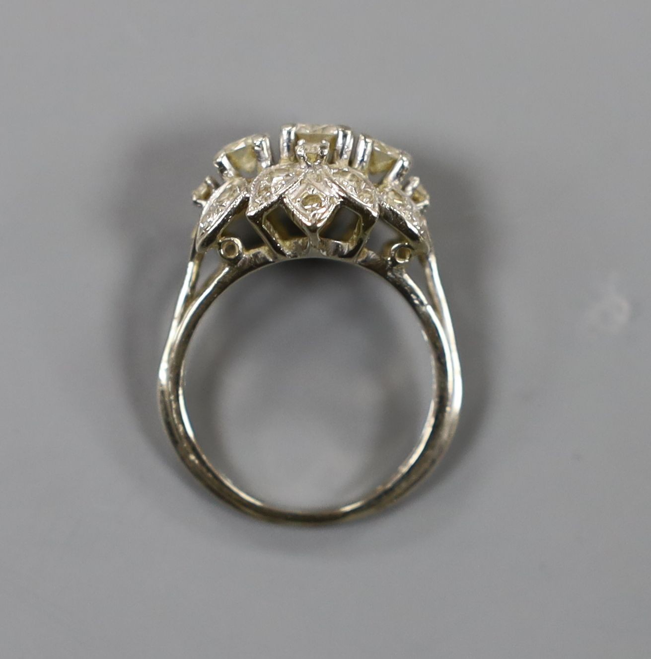 A white metal and three stone diamond ring with diamond cluster setting, size M, gross weight 4.4 grams.